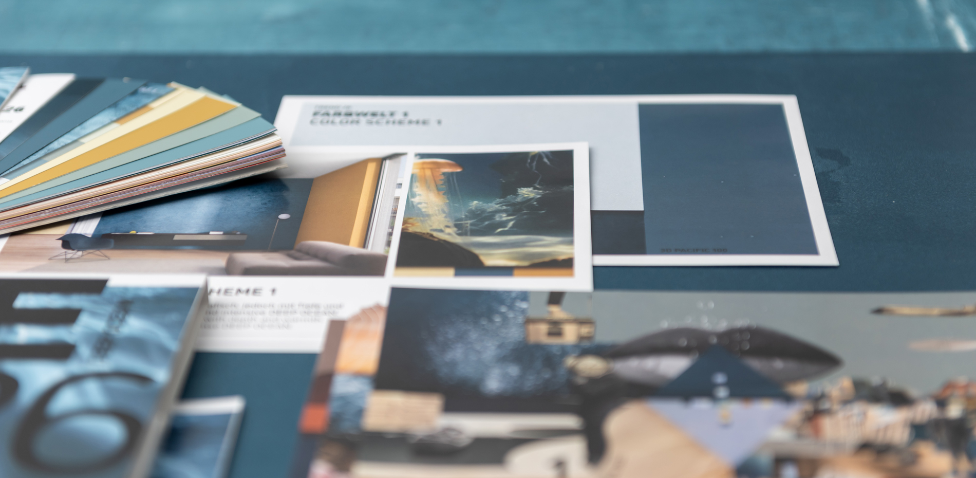 Eine Sammlung von Farbmustern, Drucksachen und Fotos liegt auf einem Tisch. Die Farbpalette besteht aus verschiedenen Blautönen, Gelbtönen und Erdtönen. Auf den Drucksachen sind Bilder und Text zu sehen, die sich mit Design- oder Konzeptthemen befassen.