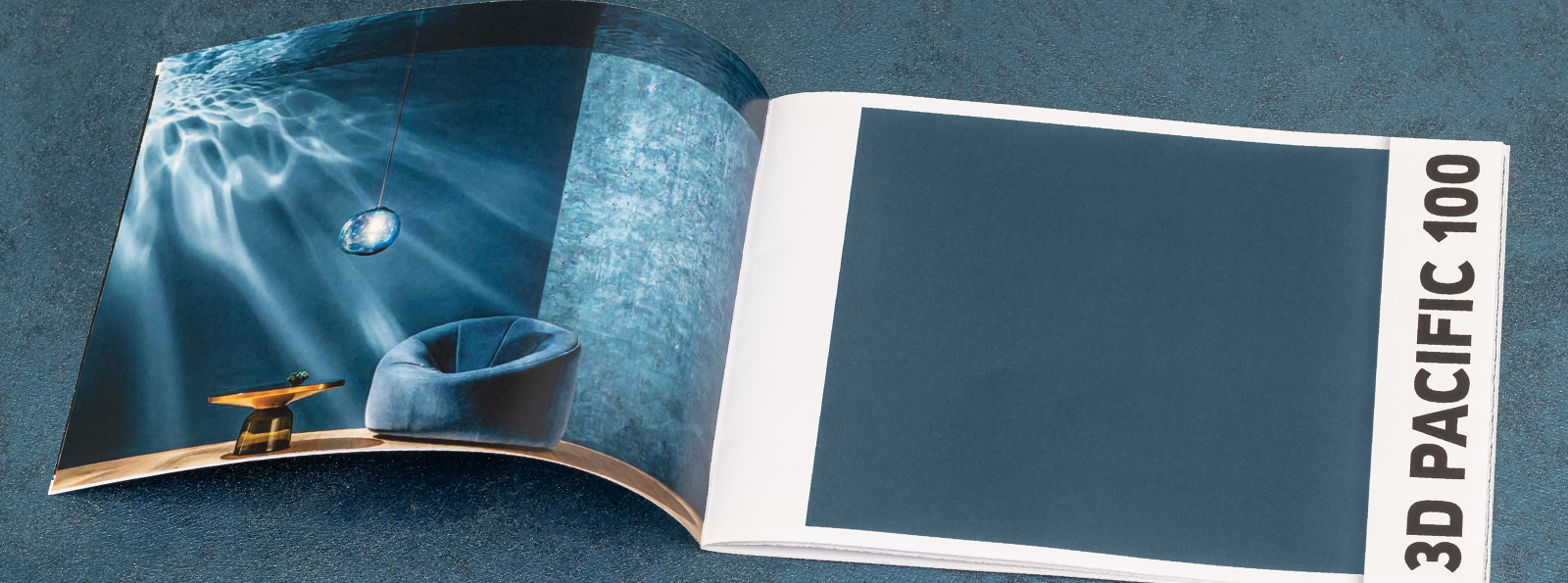 Ein offenes Buch mit einer Seite, die ein Bild einer stilvollen Lampe in einem blauen Raum zeigt, und einer leeren Seite mit der Aufschrift "3D PACIFIC 100".